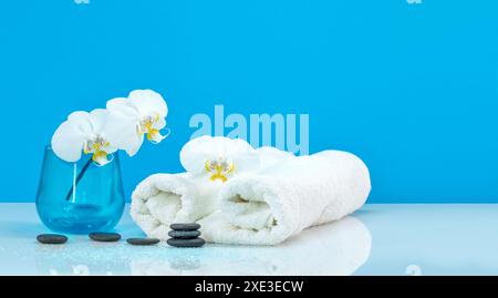 Spa Moth Orchid con asciugamano morbido e pietre per massaggi. Equilibrio di ciottoli Zen. Centro benessere e assistenza sanitaria Foto Stock