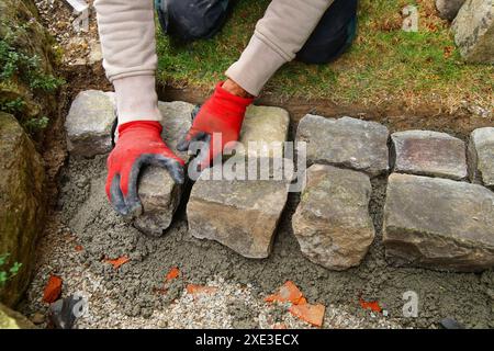 Pavimentazione in pietra naturale con pavimentazione in ciottoli. Mani indossate con i guanti di chi installa l'asfaltatrice per calcestruzzo Foto Stock