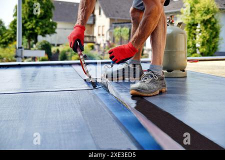 Installazione di tetti piani con torcia a soffio di propano durante i lavori di costruzione con feltro per tetti. Riscaldamento Foto Stock