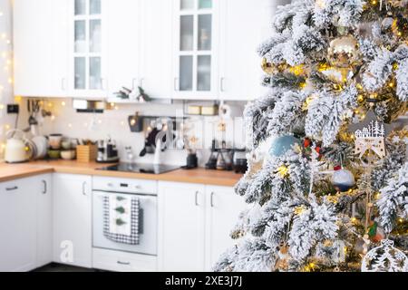 Decorazioni natalizie natalizie in cucina bianca, interni moderni in stile rustico con un albero di Natale innevato e luci fiabesche. Anno nuovo, Christm Foto Stock