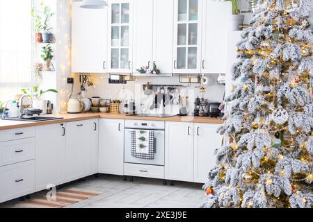 Decorazioni natalizie natalizie in cucina bianca, interni moderni in stile rustico con un albero di Natale innevato e luci fiabesche. Anno nuovo, Christm Foto Stock