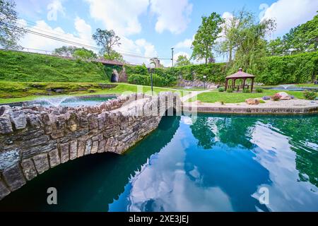 Sereno ponte in pietra e gazebo presso il laghetto riflettente nei giardini sommersi Foto Stock