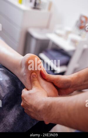 Primo piano del piede femminile con un massaggio delicato. La massaggiatrice tiene la gamba della donna nelle sue mani. Un giovane cliente mente e ama rilassarsi con un professionista Foto Stock