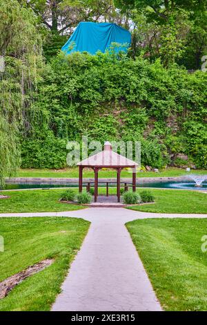 Sereno gazebo e laghetto nei lussureggianti giardini sommersi sotto cieli nuvolosi Foto Stock