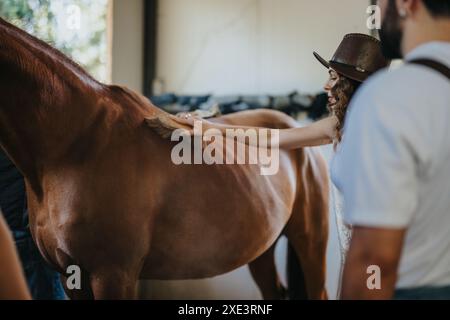 Giovane donna che si prende cura di un cavallo con un pennello in un fienile Foto Stock