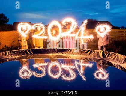 Persone con sparkler in mano che disegnano 2024 con scintille. Anno nuovo 2024, idea creativa Foto Stock