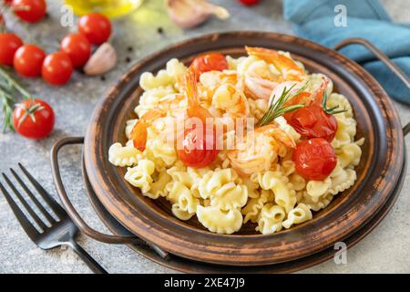 Cucina mediterranea, dieta a base di pesce. pasta italiana creste di gallo con gamberi alla griglia e pomodori su un tavolo in pietra. Foto Stock