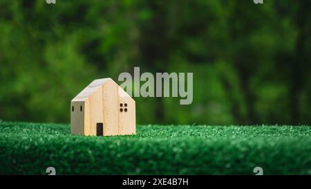 Modello di casa in legno su sfondo verde naturale, concetto di vendita di una casa, agente immobiliare offrire casa, assicurazione e sicurezza immobiliare, conveniente Foto Stock