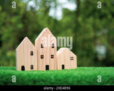 Concetto di vendita di una casa, modello di casa in legno su sfondo verde naturale, agente immobiliare offre casa, assicurazione e sicurezza immobiliare, conveniente Foto Stock