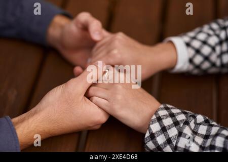 Primo piano su un uomo e una donna che si tengono per mano ad un tavolo di legno. Coppia amorevole che tiene le mani sul tavolo, uomo amico marito sostegno Foto Stock