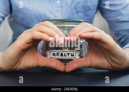 Donna che mostra il cuore con le mani segno di risparmio di denaro in vaso di vetro pieno di banconote in dollari. Trascrizione SANITARIA davanti a j Foto Stock