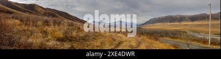 Una foto panoramica di una strada asfaltata circondata da maestose montagne nel canyon di Charyn in una giornata nuvolosa ad Almaty, Kazakistan Foto Stock