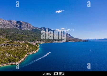 Una piccola barca con turisti galleggia lentamente su acque limpide. Costa incredibile. Fotografia aerea. Le montagne sono ricoperte di verde, il blu tran Foto Stock