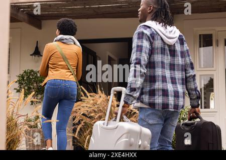 All'aperto, trasportando valigie, coppia che arriva a casa ed entra insieme in casa Foto Stock