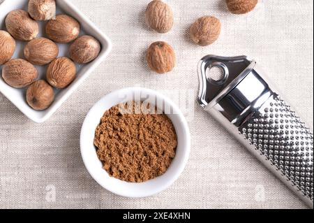 Noce moscata in polvere, macinata in una piccola ciotola bianca su tessuto di lino. Fragrante o vera noce moscata, una spezia, utilizzata anche nella medicina tradizionale. Foto Stock