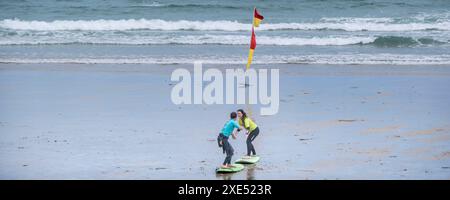 Un'immagine panoramica di un allenatore di surf della Escape Surf School e di un principiante di surf che ha una lezione di surf uno a uno sulla spiaggia di Towan a Newquay in Foto Stock