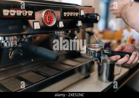 Primi piani di un barista maschile irriconoscibile che prepara una gustosa bevanda al caffè, tenendo in mano l'attrezzatura del portafiltro per caffè riempito finemente di Foto Stock