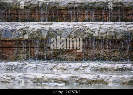 L'acqua scende giù per gradini di pietra nel parco cittadino. L'acqua sta cadendo in un flusso costante, creando un'atmosfera tranquilla e rilassante. Concetto di tranquillità Foto Stock