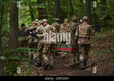 Un'unità militare d'élite, ricoperta di mimetismo, trasporta una cassa di munizioni attraverso la fitta foresta, che rappresenta la capitale strategica Foto Stock