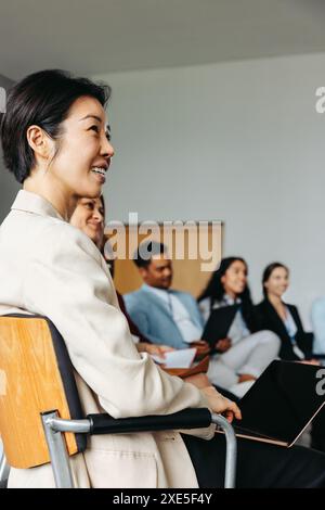 Imprenditrice di successo di etnia asiatica sorridente durante un incontro d'affari insieme ai colleghi, trasmettendo lavoro di squadra e fiducia. Foto Stock