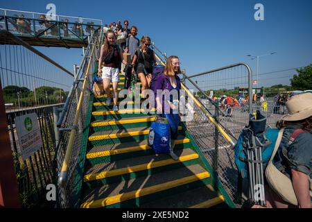 I festaioli arrivano alla stazione ferroviaria di Castle Cary mentre escono dalla piattaforma e sugli autobus che li porteranno al Glastonbury Festival presso la Worthy Farm nel Somerset. Data foto: Mercoledì 26 giugno 2024. Foto Stock