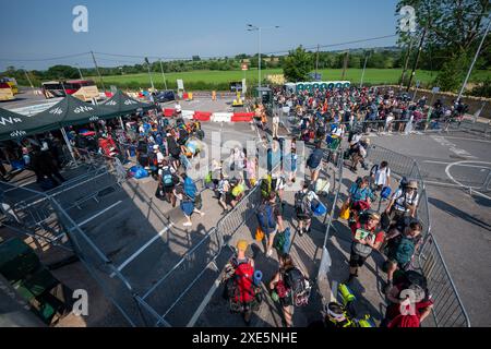 I festaioli arrivano alla stazione ferroviaria di Castle Cary mentre escono dalla piattaforma e sugli autobus che li porteranno al Glastonbury Festival presso la Worthy Farm nel Somerset. Data foto: Mercoledì 26 giugno 2024. Foto Stock