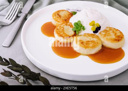 Frittelle dolci con panna acida e marmellata su un piatto bianco Foto Stock