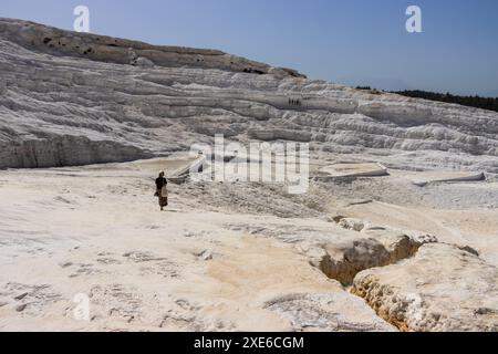 Una donna turista in cappello che cammina sulle bellissime travertini bianche di Pamukkale a Türkiye in una giornata di sole vicino all'antica città di Hierapolis. Foto Stock