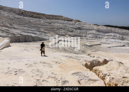 Una donna turista in cappello che cammina sulle bellissime travertini bianche di Pamukkale a Türkiye in una giornata di sole vicino all'antica città di Hierapolis. Foto Stock