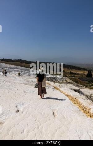 Una donna turista in cappello che cammina sulle bellissime travertini bianche di Pamukkale a Türkiye in una giornata di sole vicino all'antica città di Hierapolis. Foto Stock