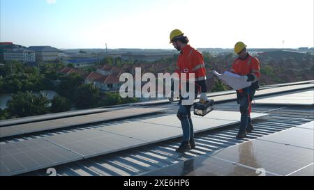 Entrambi i tecnici stanno installando pannelli solari sul tetto del magazzino per trasformare l'energia solare in energia elettrica per noi Foto Stock