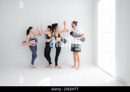 Un gruppo di atleti femminili e maschili si alzò e chiacchierò amichevolmente nello studio prima di iniziare con la lezione di yoga. Foto Stock