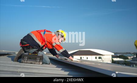 Entrambi i tecnici stanno installando pannelli solari sul tetto del magazzino per trasformare l'energia solare in energia elettrica per noi Foto Stock