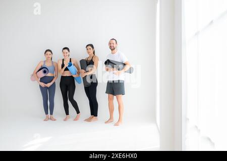 Un gruppo di atleti femminili e maschili si alzò e chiacchierò amichevolmente nello studio prima di iniziare con la lezione di yoga. Foto Stock