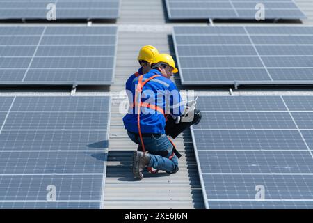 Entrambi i tecnici stanno installando pannelli solari sul tetto del magazzino per trasformare l'energia solare in energia elettrica per noi Foto Stock