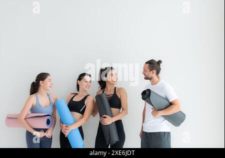 Un gruppo di atleti femminili e maschili si alzò e chiacchierò amichevolmente nello studio prima di iniziare con la lezione di yoga. Foto Stock