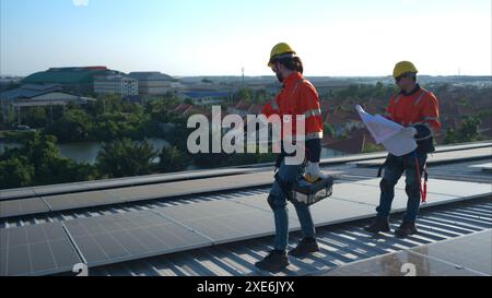 Entrambi i tecnici stanno installando pannelli solari sul tetto del magazzino per trasformare l'energia solare in energia elettrica per noi Foto Stock