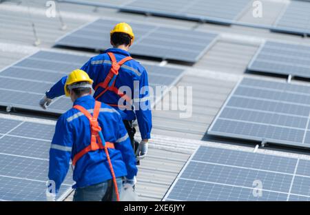 Entrambi i tecnici stanno installando pannelli solari sul tetto del magazzino per trasformare l'energia solare in energia elettrica per noi Foto Stock