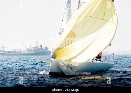 I marinai manovrano una barca a vela durante una regata con uno spinnaker che cattura il vento Foto Stock