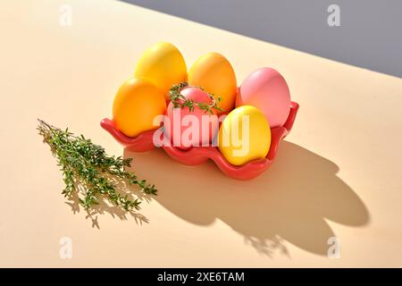 Uova di Pasqua nelle tonalità rosa, giallo e arancione su un banco rosso. Foto Stock