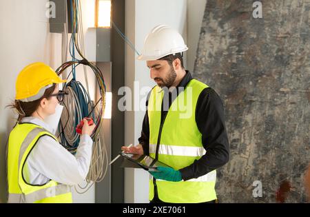 Ingegneri maschi e femmine che lavorano nel cantiere, stanno monitorando l'impianto elettrico dell'edificio. Foto Stock