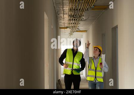 Ingegneri maschi e femmine che lavorano nel cantiere, stanno monitorando l'impianto elettrico dell'edificio. Foto Stock