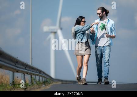 Giovani coppie che si rilassano vicino alla turbina eolica sul lago Foto Stock