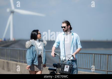 Giovani coppie che si rilassano vicino alla turbina eolica sul lago Foto Stock