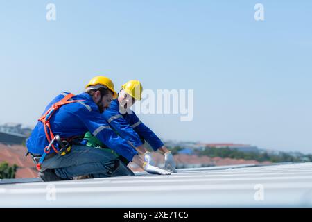 Entrambi i tecnici stanno installando pannelli solari sul tetto del magazzino per trasformare l'energia solare in energia elettrica per noi Foto Stock