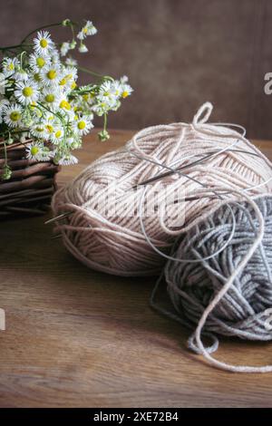 Palle di filato e cesto di datteri bianchi su un tavolo di legno. Hobby per lavorare a maglia. Filati di lana e aghi per maglieria con fiori. Interni accoglienti. Concetto di cucitura. Foto Stock