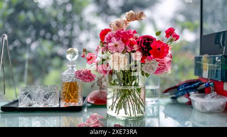Bellissimo bouquet di rose selvatiche in un vaso di vetro accanto a un decanter e 2 bicchieri di cristallo sullo sfondo della finestra, luce naturale Foto Stock