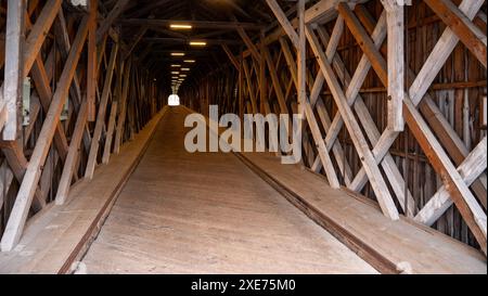 Vista interna di un ponte coperto in legno con travi incrociate e una prospettiva a punto di svanimento. Foto Stock