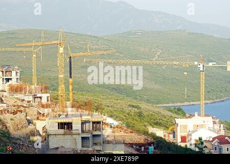 Vista del cantiere: Numerose gru a torre e ville in cemento sullo sfondo di verdi montagne Foto Stock