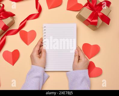 Apri il notebook con fogli bianchi vuoti e confezioni regalo su sfondo giallo, vista dall'alto. Foto Stock